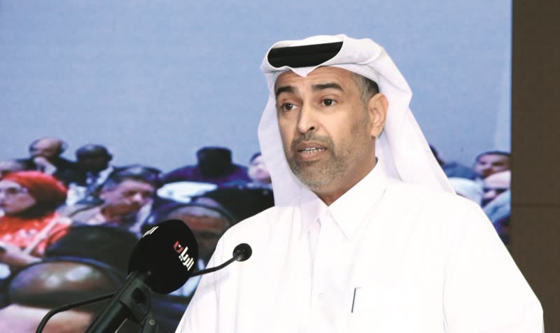 A Qatari official speaks at the lectern during the first ESG Qatar conference in 2024, a live feed of the seated audience on the screen behind him.