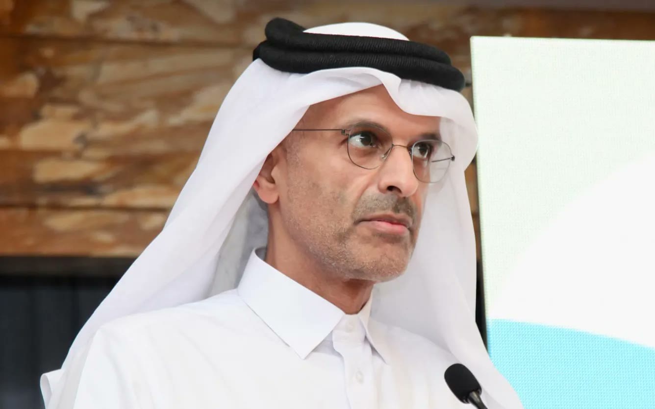 A Qatari official in a white thobe speaking at the lectern microphone during ESG Qatar 2025.